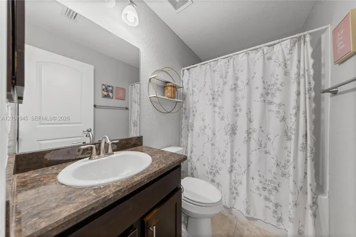 Dark wood vanity with a stone-finish countertop, undermount oval sink, chrome dual-handle faucet, and large wall-mounted mirror