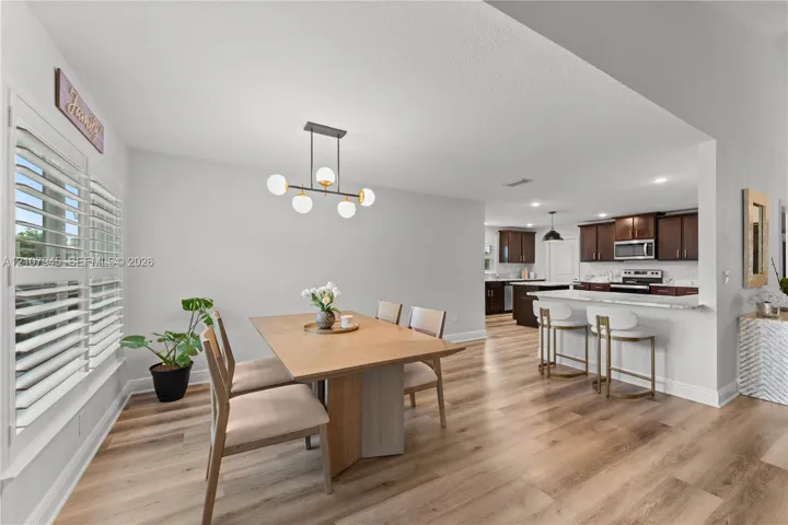 Dining area featuring wood-finish flooring, a contemporary six-light globe chandelier, and white plantation shutters