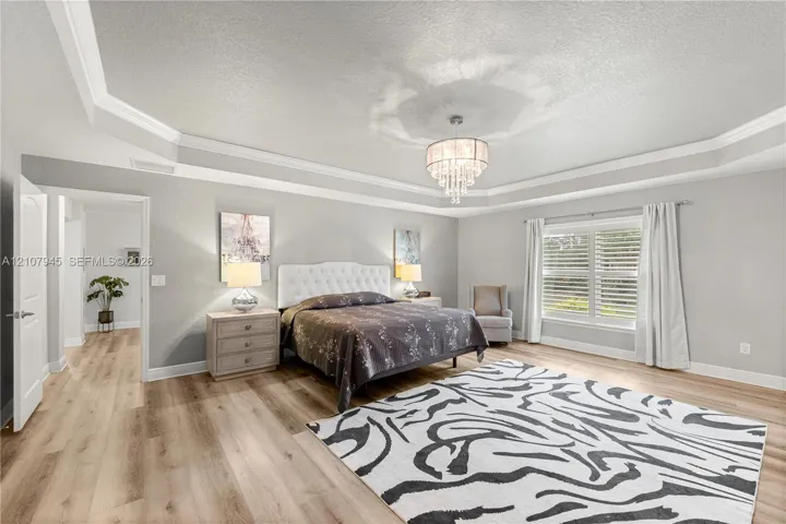 Tray ceiling with crown molding, crystal-style chandelier, wood-finish flooring, and multi-pane windows with horizontal blinds