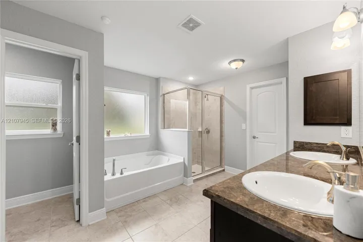 Bathroom featuring a dual-sink vanity with a dark-finish cabinet and solid-surface countertop, a separate deep soaking tub, and a glass-enclosed shower
