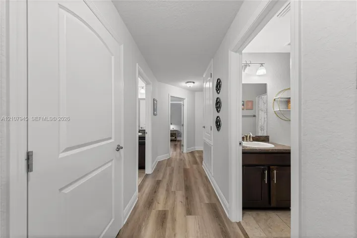 Interior hallway featuring wood-finish flooring, two-panel interior doors, and a bathroom equipped with a vanity, stone-finish countertop, and integrated sink