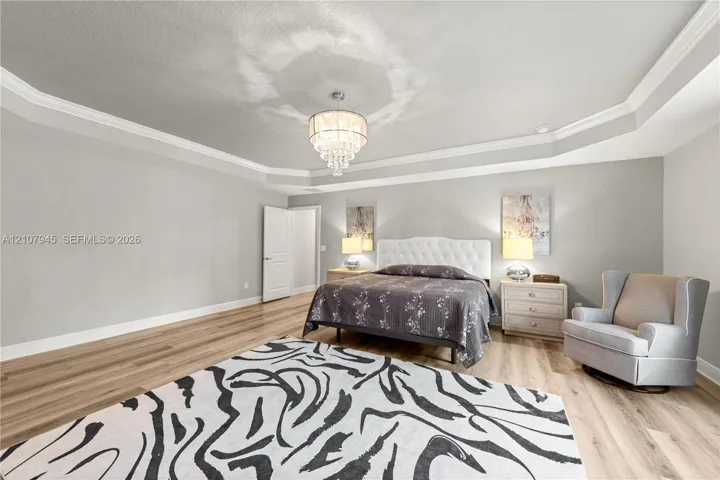 Tray ceiling featuring multi-tiered crown molding, wood-finish flooring, and a crystal chandelier