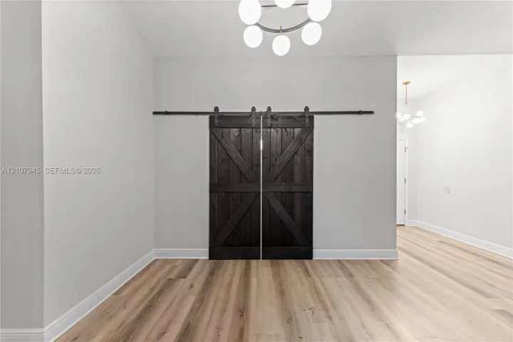 Double sliding barn doors with a dark wood finish and black hardware, complemented by wood-finish flooring and a multi-bulb geometric chandelier