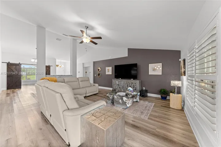 Vaulted ceilings, wood-finish flooring, accent wall, ceiling fan, and plantation shutters