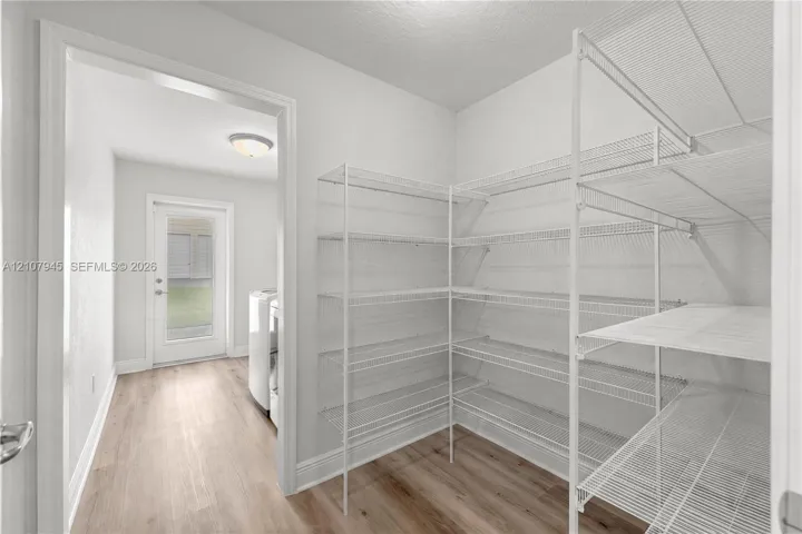 Storage room featuring white wire shelving and wood-finish flooring, with a doorway leading to a utility space with a glass-paneled exterior door