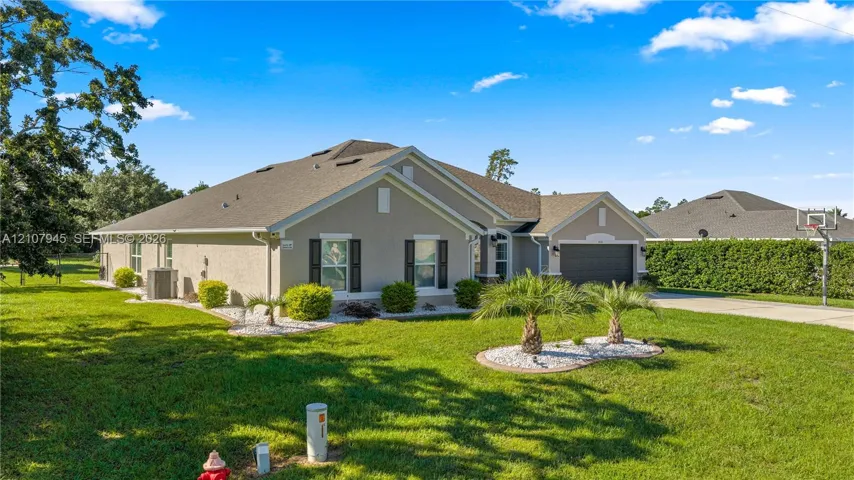 Single-story residence featuring a stucco exterior, shingle roof, attached two-car garage, manicured lawn with ornamental palm landscaping, and concrete driveway