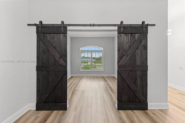 Dark-stained wood barn doors featuring matte black hardware, arched window with shutters, and wood-finish flooring