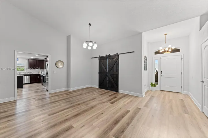 Open-concept area featuring wood-finish flooring, high ceilings, sliding barn-style doors, and decorative pendant lighting