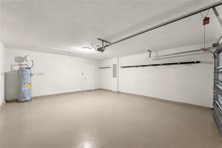 Attached garage featuring painted concrete flooring, wall-mounted storage rack, overhead lighting, and dedicated water heater housing