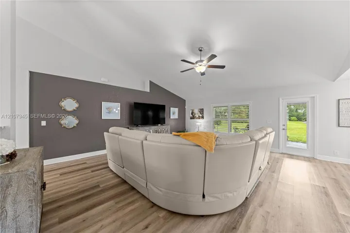 Vaulted ceilings featuring a central light-integrated ceiling fan, wood-finish flooring, and a glass-paneled exterior door