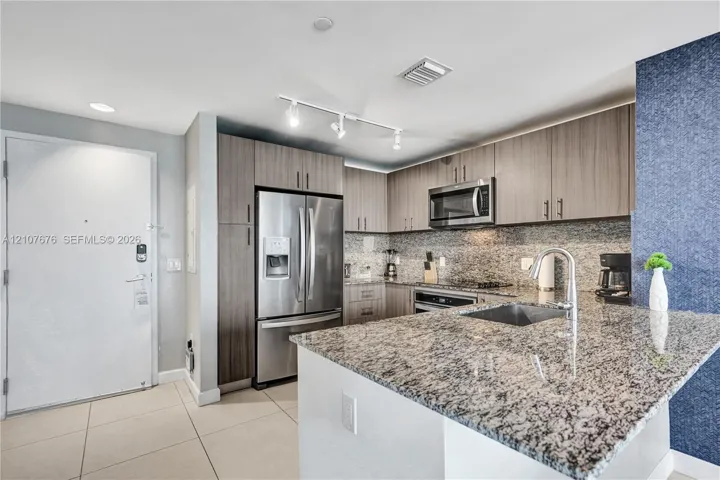 Kitchen featuring stone countertops, stainless steel appliances, flat-panel cabinetry, track lighting, and a prep sink