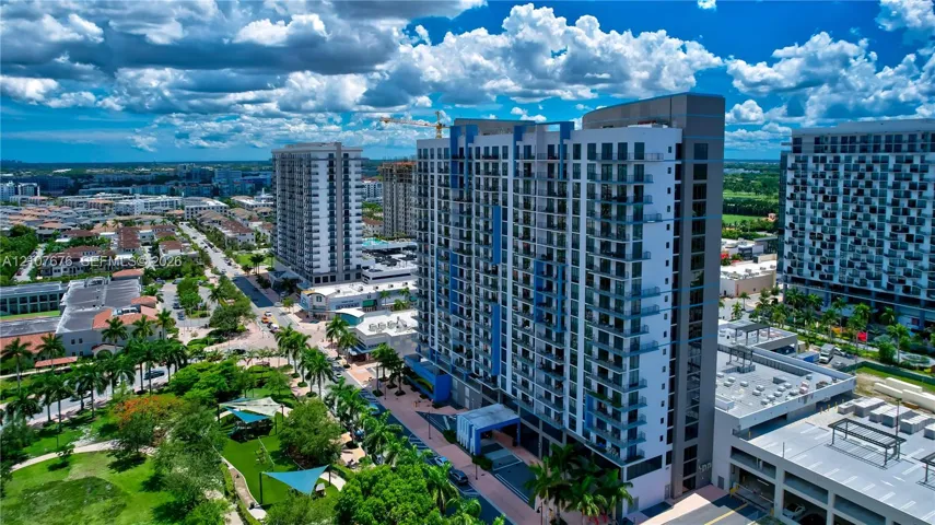 High-rise architectural structure featuring a grid glass facade and individual balconies, situated in a dense urban environment with surrounding multi-story developments and paved pedestrian access