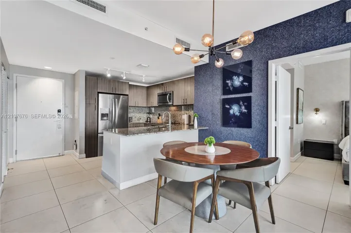 Kitchen featuring stainless steel appliances, stone countertops, and wood-finish cabinetry, complemented by a multi-bulb modern chandelier and a textured accent wall