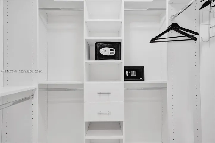 Custom walk-in closet featuring white laminate built-in cabinetry, adjustable shelving, dual soft-close drawers with silver-tone pulls, and integrated garment rods