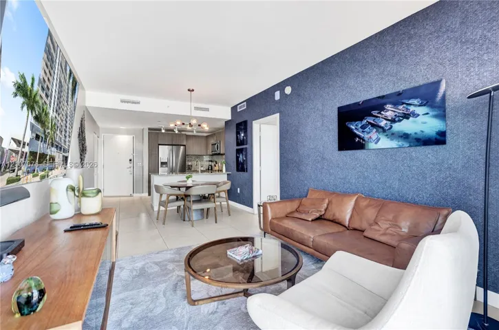 Open-concept living space featuring large-format tile flooring, a prominent textured navy accent wall, stainless steel kitchen appliances, and a contemporary multi-light chandelier