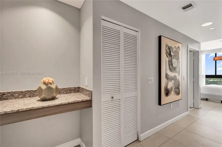 Built-in stone-surface desk with wood-finish trim, bi-fold louvered closet doors, and large-format tile flooring
