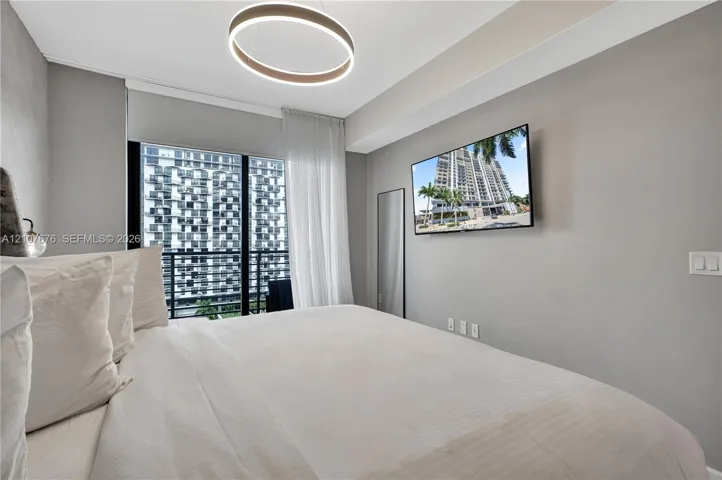 Floor-to-ceiling glass sliding doors opening to a private balcony, contemporary circular LED chandelier, and wall-mounted television