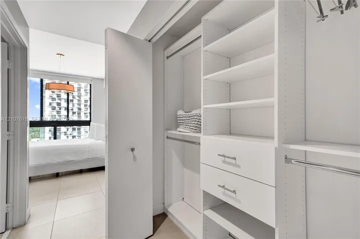 Custom reach-in closet featuring white built-in shelving, dual soft-close drawers, metal garment rods, and integrated cabinetry hardware