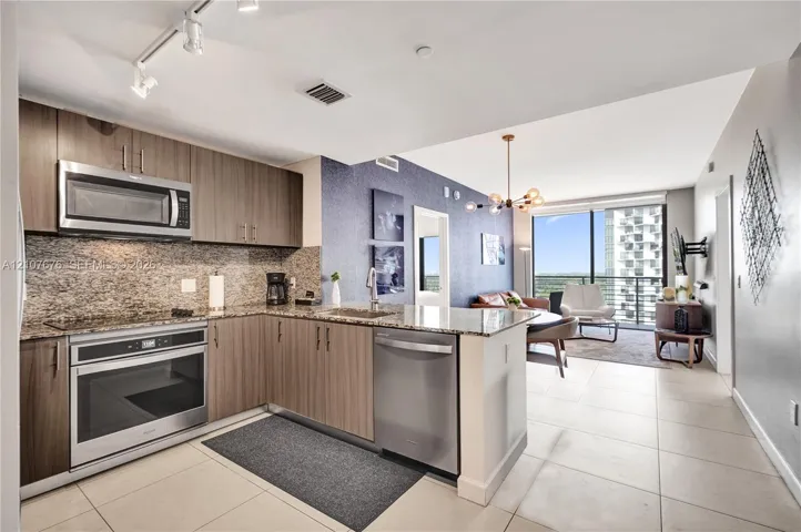 Kitchen featuring wood-finish cabinetry, stone-surface countertops, stainless steel appliances, track lighting, and tile flooring