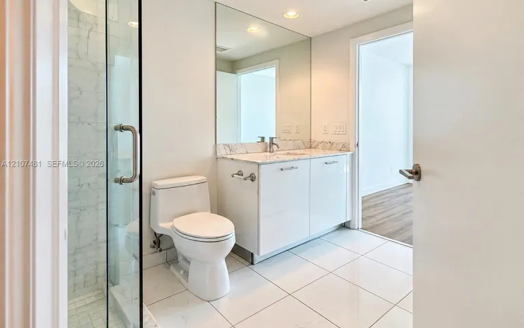 Bathroom featuring a glass-enclosed shower, stone-finish countertop, white cabinetry, wall-to-wall vanity mirror, and large-format tile flooring