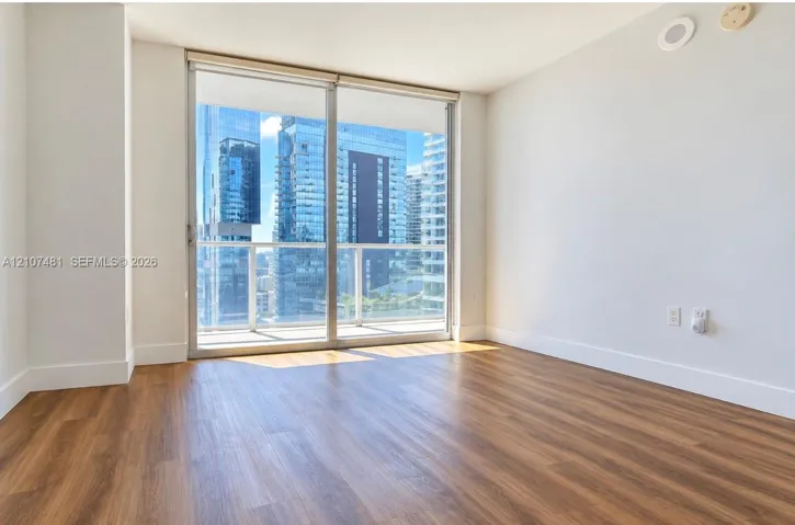 Floor-to-ceiling sliding glass door, private balcony with metal railing, and wood-finish flooring