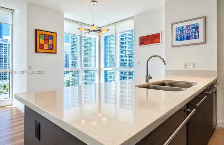 Kitchen island featuring a stone-surface countertop, double-basin stainless steel undermount sink, gooseneck faucet, dark-finish cabinetry, and floor-to-ceiling windows