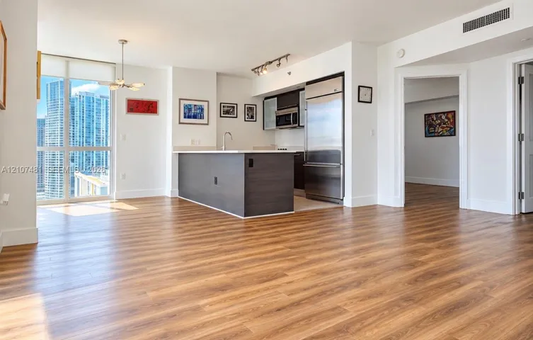Open-concept kitchen featuring dark wood-finish cabinetry, stainless steel appliances, and a central island with a solid-surface countertop, complemented by wood-finish flooring and floor-to-ceiling windows