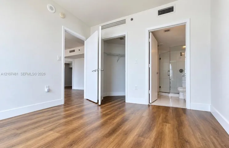 Wood-finish flooring, interior doors with lever-style hardware, reach-in closet, and an en suite bathroom featuring a glass-enclosed shower