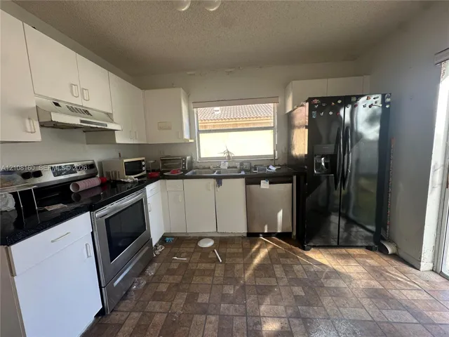 Kitchen featuring white cabinetry, dark countertops, a stainless steel range and dishwasher, and a black refrigerator