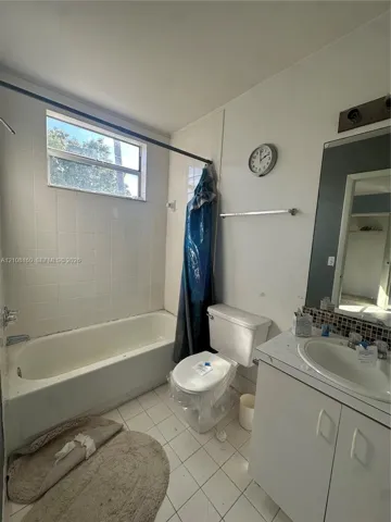 Bathroom featuring white tiled tub surround, rectangular window, vanity with integrated basin, mosaic tile backsplash, and wall-mounted vanity mirror