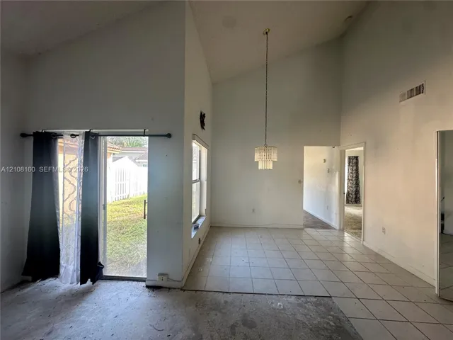 Vaulted ceilings featuring a suspended tiered chandelier, large window, and sliding glass door with exterior access