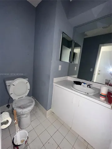 Bathroom featuring a white vanity cabinet, solid-surface countertop with an integrated oval sink, single-handle faucet, large wall-mounted mirror, and tile flooring