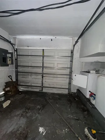 Enclosed garage space featuring a paneled sectional garage door, concrete flooring, and an integrated electrical service panel