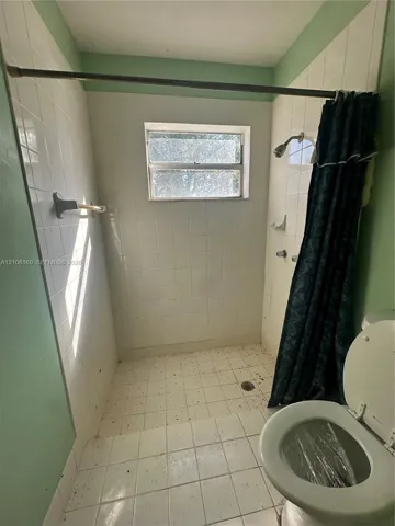Walk-in shower enclosure featuring white square tile surround, integrated soap dish, chrome shower head, and central window