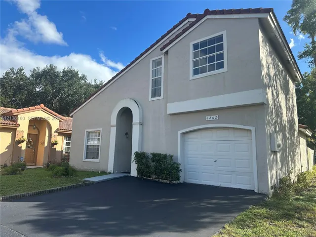 Two-story exterior featuring a stucco facade, tiled roof, arched entryway, and an attached single-car garage with a paved driveway