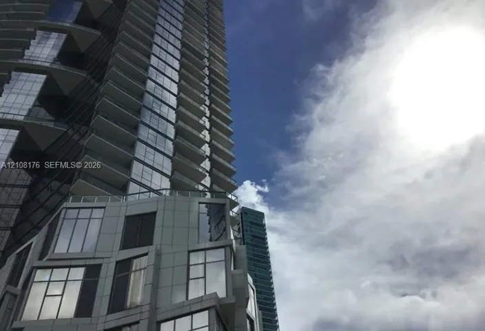 High-rise tower exterior featuring a glass and metal facade, geometric structural articulation, and wrap-around balconies with glass railings