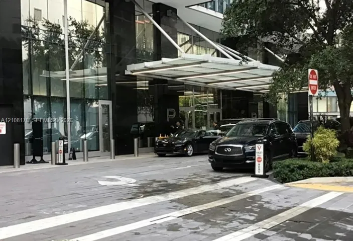 Contemporary building exterior featuring a polished black stone facade, expansive floor-to-ceiling glass paneling, and a cantilevered architectural canopy over a paved motor court