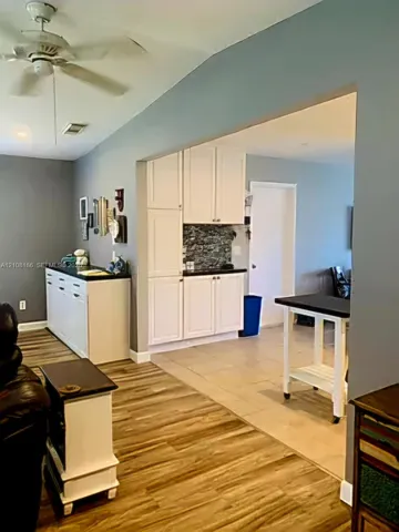White shaker-style cabinetry with dark countertops, textured stone-look backsplash, wood-finish flooring, and ceiling fan with integrated lighting