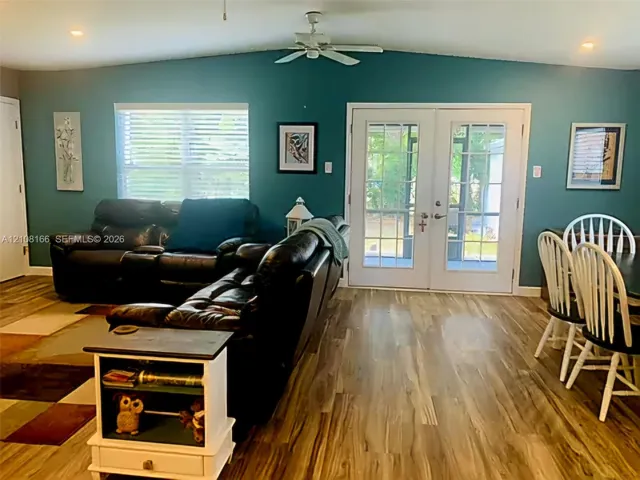 Vaulted ceiling with integrated paddle fan, wood-finish flooring, and glass-paneled double doors providing outdoor access