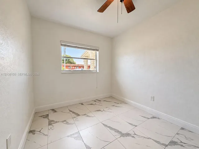 Room featuring large-format tile flooring with a neutral veined pattern, smooth wall finishes, a single-hung window, and a ceiling-mounted fan with wood-finish blades
