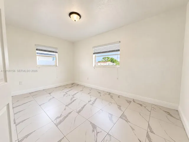 Room featuring large-format tile flooring with veining, two windows with horizontal blinds, and a centered flush-mount light fixture