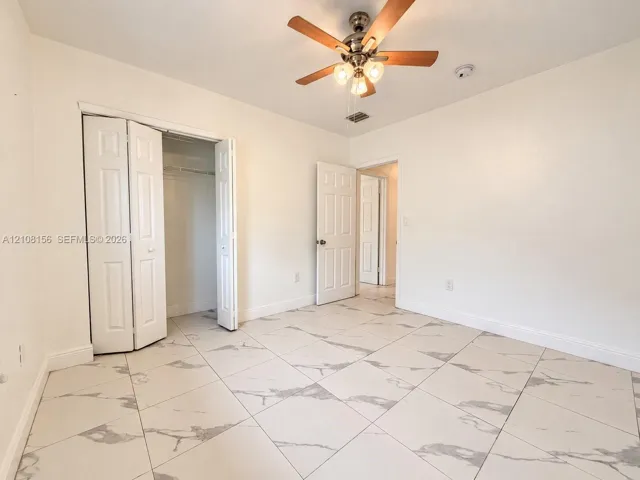 Neutral-toned interior featuring large-format tile flooring with a marble-finish pattern, a ceiling-mounted light fixture with a fan, and bi-fold closet doors