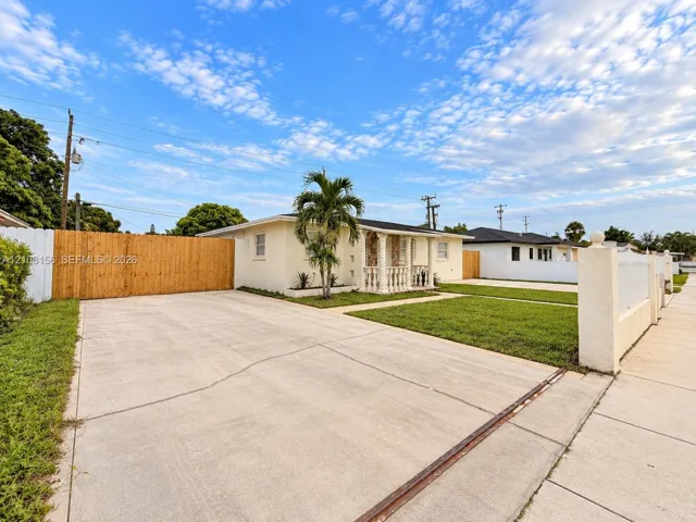 Single-story exterior featuring a concrete driveway, gated wooden fence, front covered porch with decorative columns, and manicured lawn