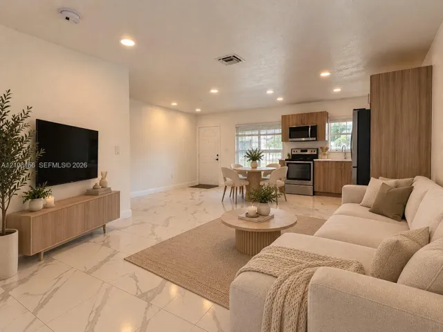 Large-format tile flooring with marble-style veining, recessed lighting, and kitchen featuring wood-finish cabinetry, stainless steel appliances, and built-in pantry storage