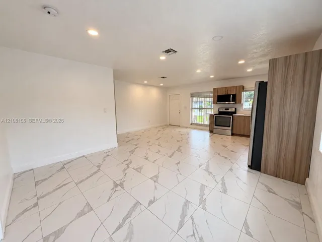 Large-format stone-style tile flooring, recessed lighting, wood-finish cabinetry, stainless steel kitchen appliances, and neutral wall tones