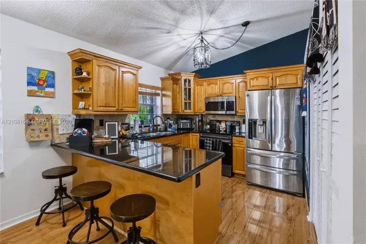 Kitchen featuring wood cabinetry, dark stone-finish countertops, stainless steel appliances, wood-finish flooring, and a vaulted ceiling