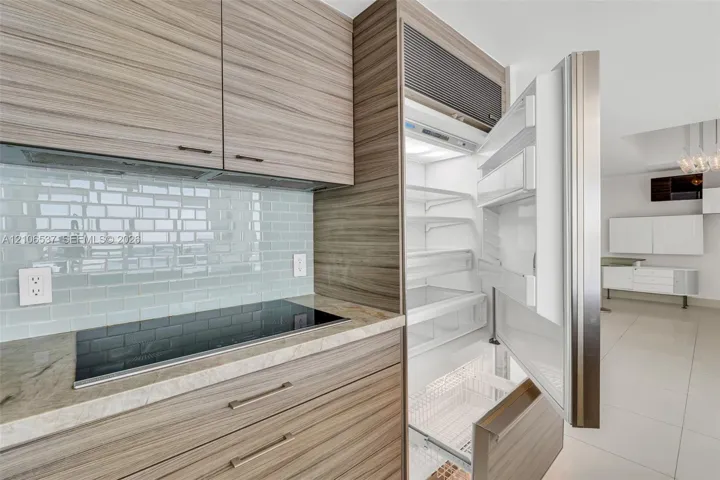 Custom wood-finish cabinetry, built-in integrated refrigerator, stone countertop, induction cooktop, and glass tile backsplash