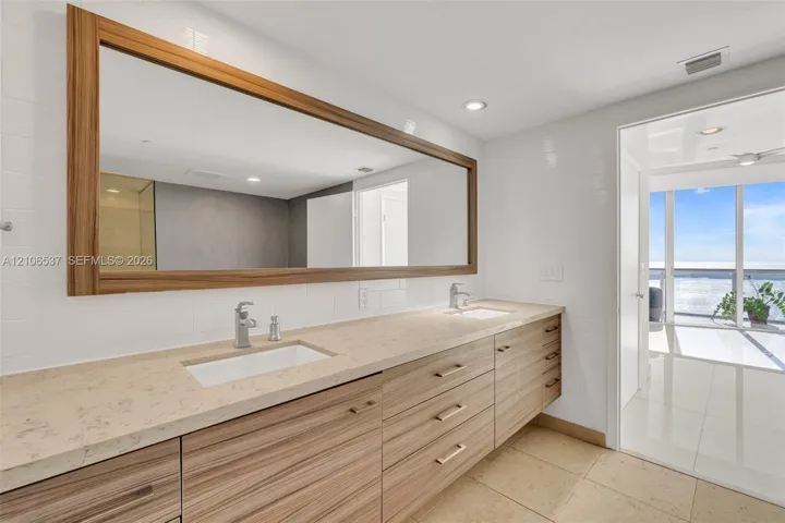 Dual-sink floating vanity with wood-finish cabinetry, stone countertop, integrated rectangular sinks, and an oversized wood-framed mirror