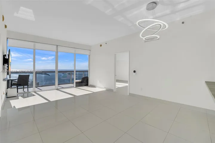 Living area featuring large-format tile flooring, floor-to-ceiling glass sliding doors, a metal-railing balcony, and a contemporary multi-ring LED chandelier
