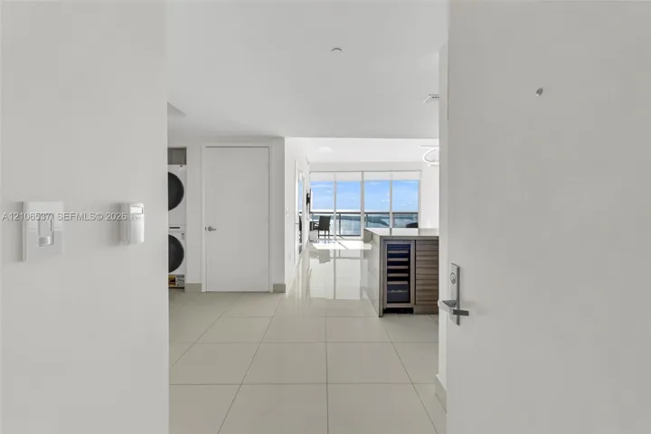 Large-format tile flooring, built-in wine refrigerator, wood-finish kitchen cabinetry, stacked laundry unit, and floor-to-ceiling windows